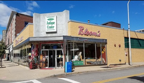 A vintage-style storefront featuring "Bloom's" and an "Antique Center" sign, with large windows and outdoor seating.