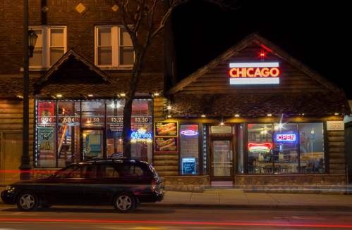 A Chicago-style restaurant at night, featuring neon signs and a parked car outside. Warm lights illuminate the entrance.