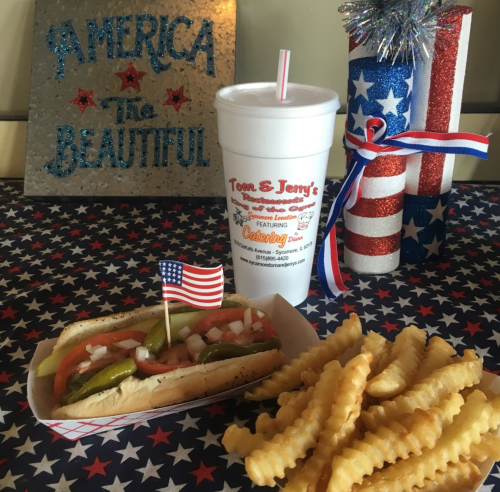 A festive table with a hot dog topped with pickles and onions, crinkle-cut fries, and a drink, all decorated for a celebration.
