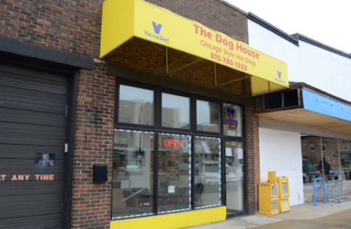 Exterior of "The Dog House," a hot dog restaurant with a bright yellow awning and an "Open" sign.