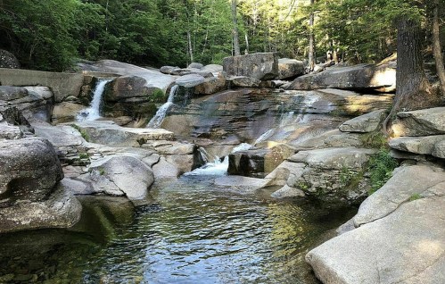 A serene landscape featuring cascading waterfalls over smooth rocks, surrounded by lush green trees.