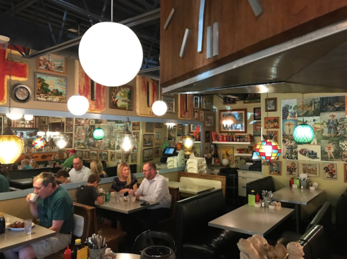 A cozy diner with colorful decor, featuring booths, tables, and vintage artwork on the walls. Patrons enjoy their meals.