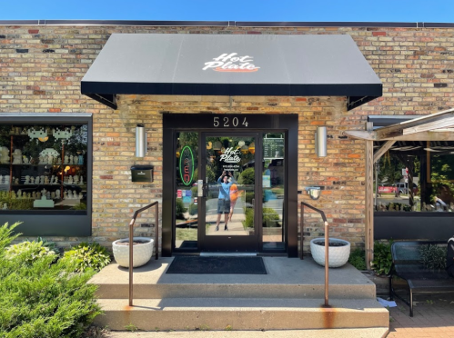 Exterior of Hot Plate restaurant with a brick facade, awning, and entrance steps, surrounded by greenery.