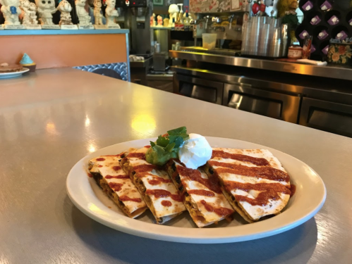 A plate of quesadillas drizzled with sauce, topped with sour cream and cilantro, on a table in a colorful restaurant.