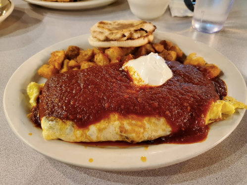 A plate of omelette topped with red sauce and sour cream, served with potatoes and an English muffin.