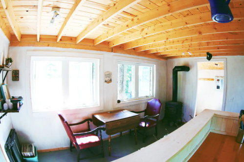 Cozy interior with wooden ceiling, two red chairs, a small table, and large windows letting in natural light.