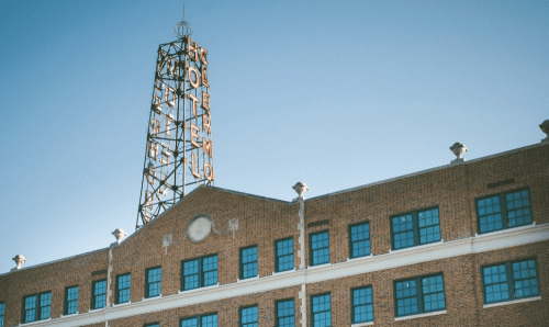 Historic brick building with a tall, illuminated sign reading "Polermo" against a clear blue sky.