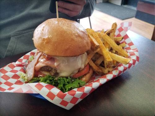 A large burger with lettuce, tomato, cheese, and bacon, served with a side of golden fries in a checkered basket.