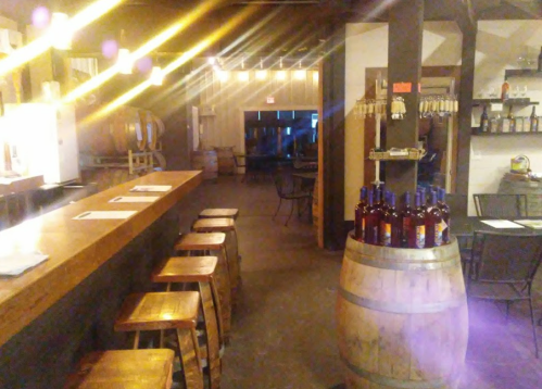 A rustic bar interior with wooden stools, a barrel, and warm lighting, creating a cozy atmosphere.