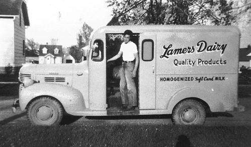 A vintage dairy delivery truck with a man standing at the door, labeled "Lamers Dairy Quality Products."