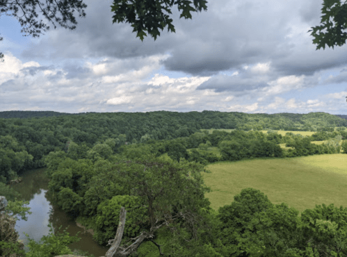 A scenic view of lush green hills and a river under a cloudy sky.