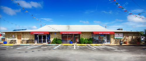 A stone building with red awnings for a restaurant and bar, surrounded by a clear blue sky and festive decorations.