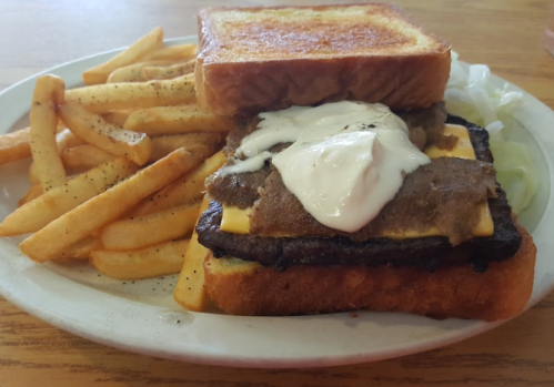 A plate with a sandwich made of toasted bread, ground beef, cheese, and mayonnaise, served with French fries.