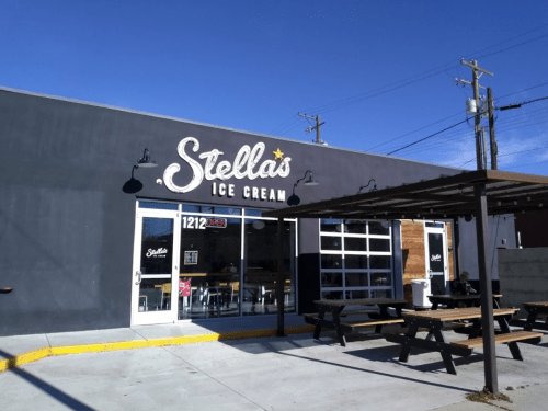 Exterior of Stella's Ice Cream shop with a sign, outdoor seating, and a clear blue sky.