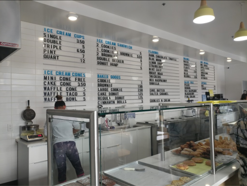 A menu board at an ice cream shop displays prices for ice cream cups, sandwiches, and baked goods.