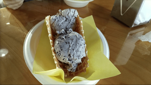 A waffle cone filled with two scoops of purple ice cream on a yellow napkin, placed on a wooden table.