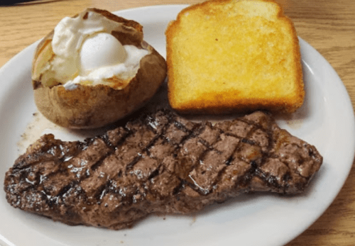 A plate with a grilled steak, a baked potato topped with sour cream, and a slice of toasted bread.