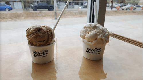 Two cups of ice cream from Stella's: one with brown caramel flavor and the other with white vanilla, placed on a wooden table.