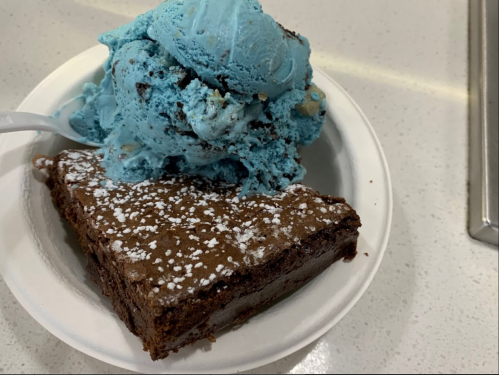 A bowl with a slice of chocolate brownie topped with powdered sugar and a scoop of blue ice cream.