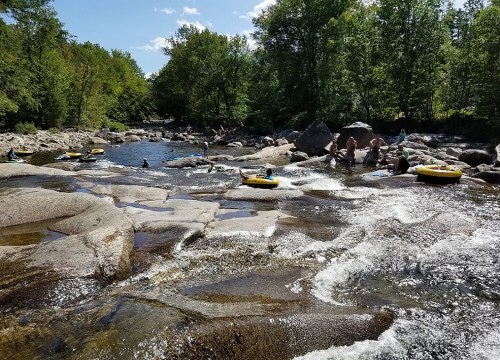 People relaxing and tubing on a rocky river surrounded by lush greenery and blue skies.