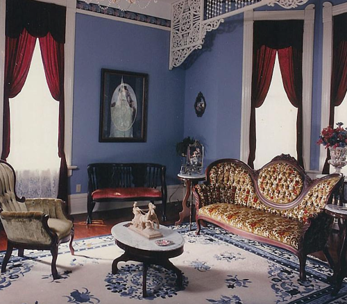 Victorian-style living room with ornate furniture, a patterned rug, and decorative curtains in a blue-walled setting.