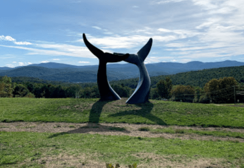 A large black sculpture of two hands reaching towards each other, set against a backdrop of mountains and blue sky.