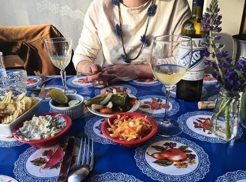 A colorful table setting with drinks, appetizers, and a person’s hands, featuring vibrant dishes and decorative tablecloth.