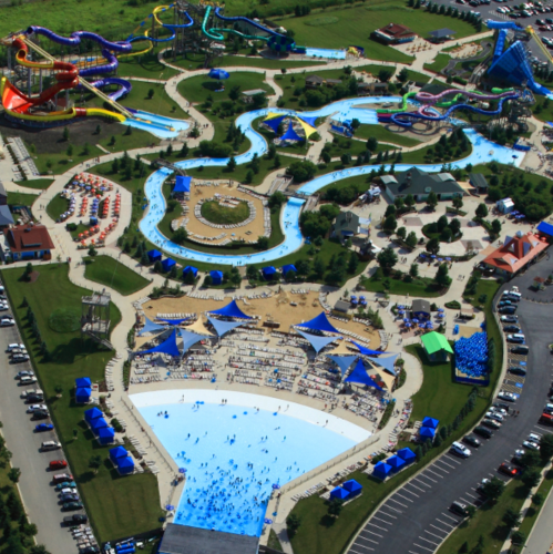 Aerial view of a large water park featuring slides, pools, and sunbathing areas, with many visitors enjoying the attractions.