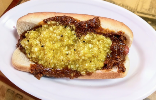 A hot dog in a bun topped with a thick layer of yellow relish and a dark brown sauce.