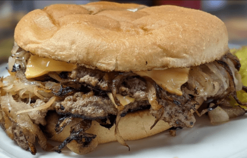 A hearty sandwich with layers of beef, melted cheese, and sautéed onions on a soft bun, served on a plate.