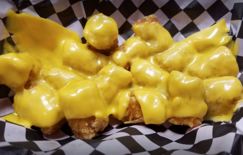 A serving of crispy tater tots smothered in melted yellow cheese, served in a black and white checkered paper.