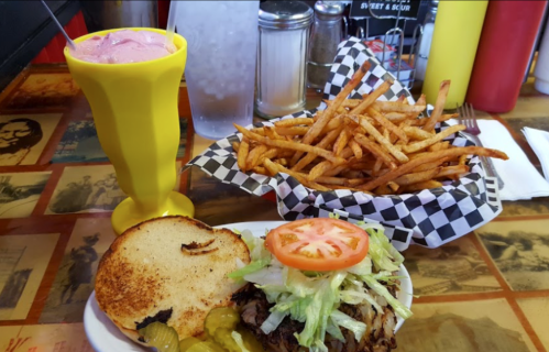 A colorful meal featuring a sandwich with lettuce and tomato, a side of crispy fries, and a pink drink in a yellow cup.