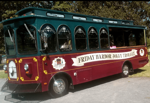 A colorful trolley bus with "Friday Harbor Jolly Trolley" signage parked on a gravel surface.