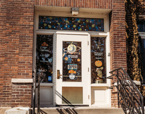 Entrance of a children's museum with colorful decorations on the door and a welcoming "Open" sign.