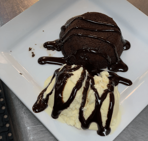 A plate with a chocolate lava cake drizzled with chocolate sauce, served alongside a scoop of vanilla ice cream.