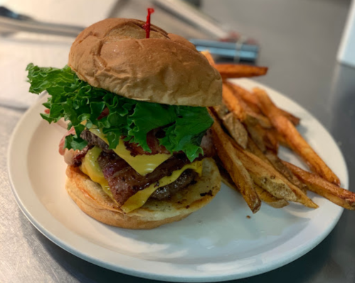 A juicy burger with lettuce, cheese, and bacon, served with a side of crispy fries on a white plate.