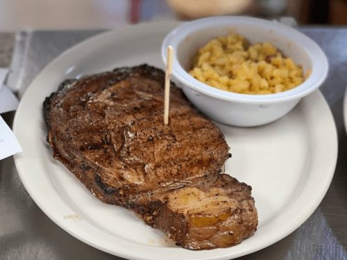 A large, grilled steak on a plate with a side of macaroni and cheese in a bowl.