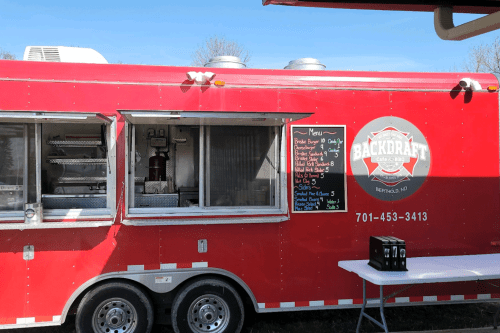 A red food truck with a menu board, parked outdoors under a clear blue sky.