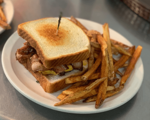 A toasted sandwich with bacon and mustard, served with a side of golden French fries on a white plate.