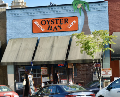 Exterior of Oyster Bay Seafood Cafe with a palm tree sign, open for business, and a hiring notice displayed.