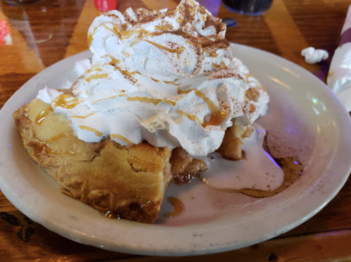 A slice of pie topped with whipped cream, drizzled with caramel, served on a plate.