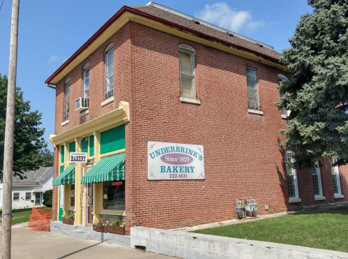 A brick building with green awnings and a sign reading "Underbrink's Bakery Since 1929." Trees and blue sky in the background.