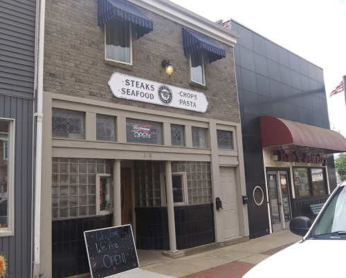A restaurant with a sign reading "Steaks, Seafood, Chops, Pasta" and an open sign, next to a jewelry store.
