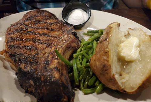 A grilled steak with green beans and a baked potato topped with butter, served on a white plate.