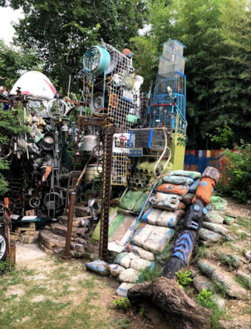 A colorful, eclectic sculpture garden made from recycled materials, featuring various objects stacked creatively.