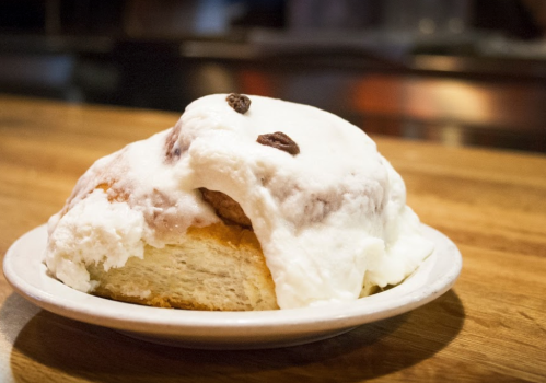 A large cinnamon roll topped with white icing and a few raisins, served on a small plate.