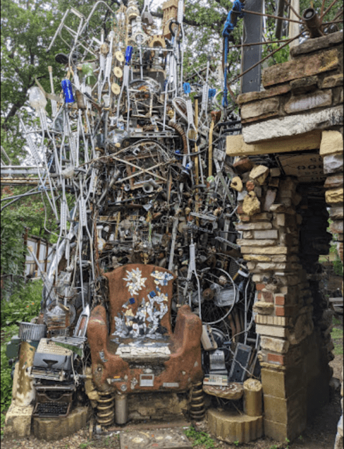 A towering sculpture made of various metal objects and tools, resembling a chaotic, artistic installation.