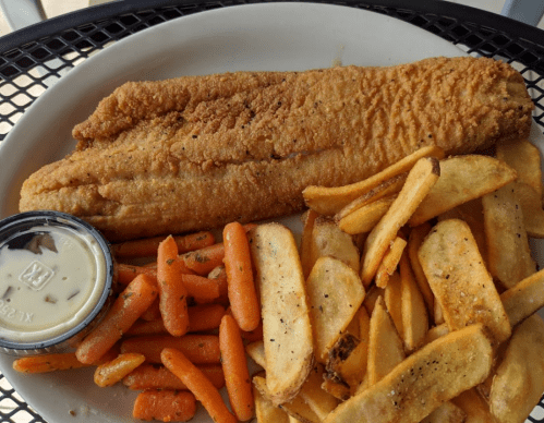 A plate with a fried fish fillet, golden fries, and seasoned carrots, accompanied by a small container of dipping sauce.