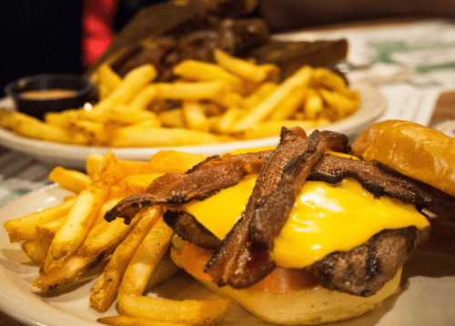 A close-up of a cheeseburger topped with bacon, served with a side of golden French fries.