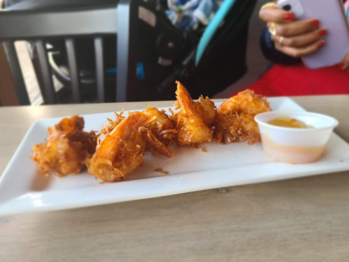 A plate of crispy fried shrimp with a small cup of dipping sauce on a wooden table.
